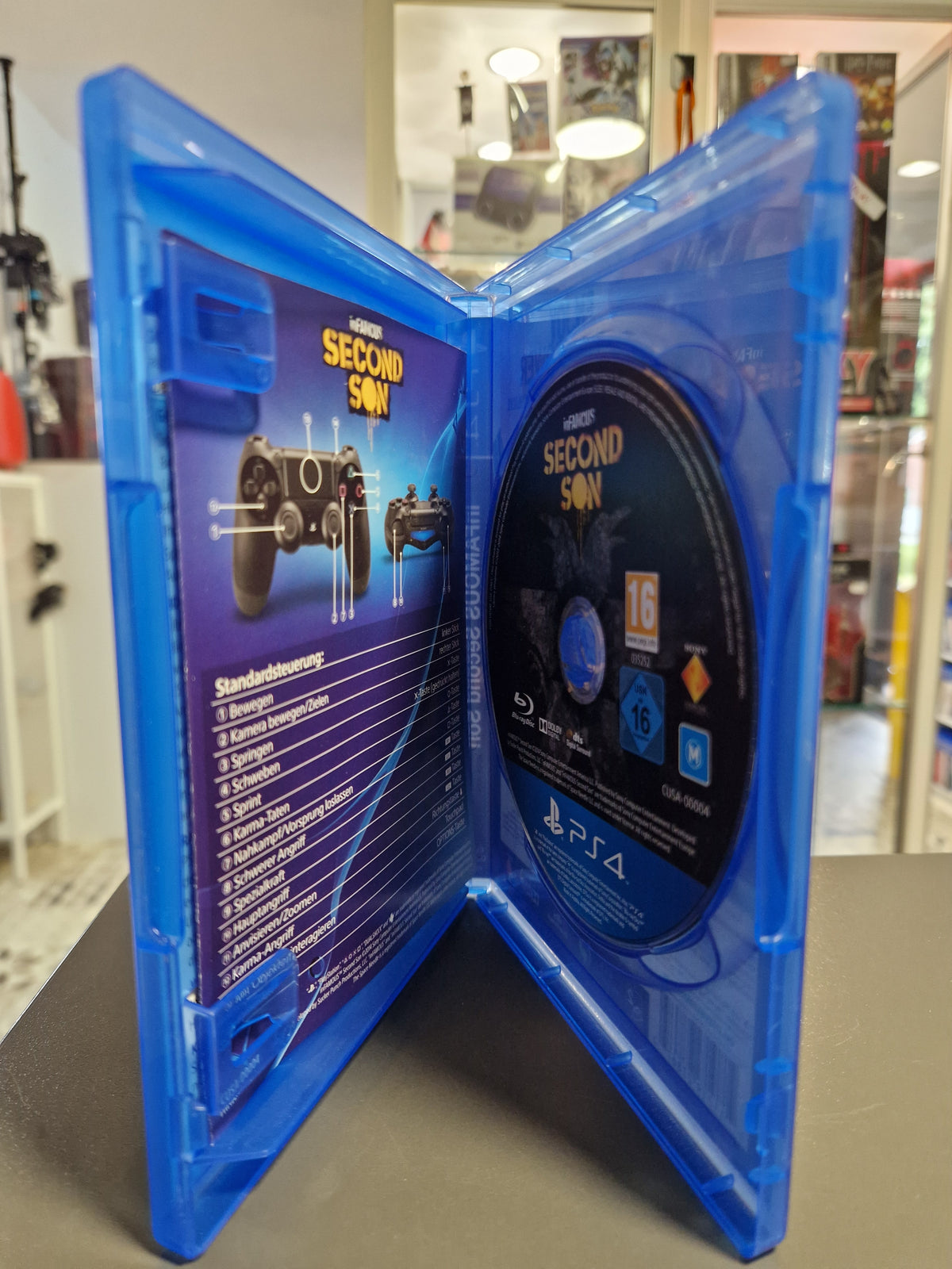 Geöffnete PlayStation 4 Hülle von inFAMOUS Second Son mit Blu-ray Disc und Steuerungsbeilage.