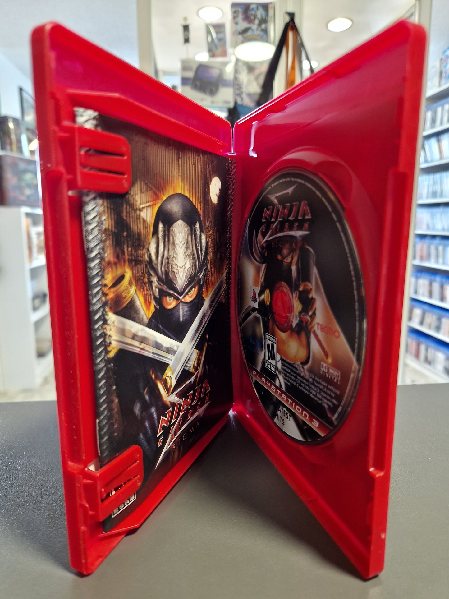 Die geöffnete, rote PS3 Hülle zeigt die originale, farbige Spielanleitung auf der linken Seite und die saubere, kratzerfreie Ninja Gaiden Sigma Spieldisc auf der rechten Seite.