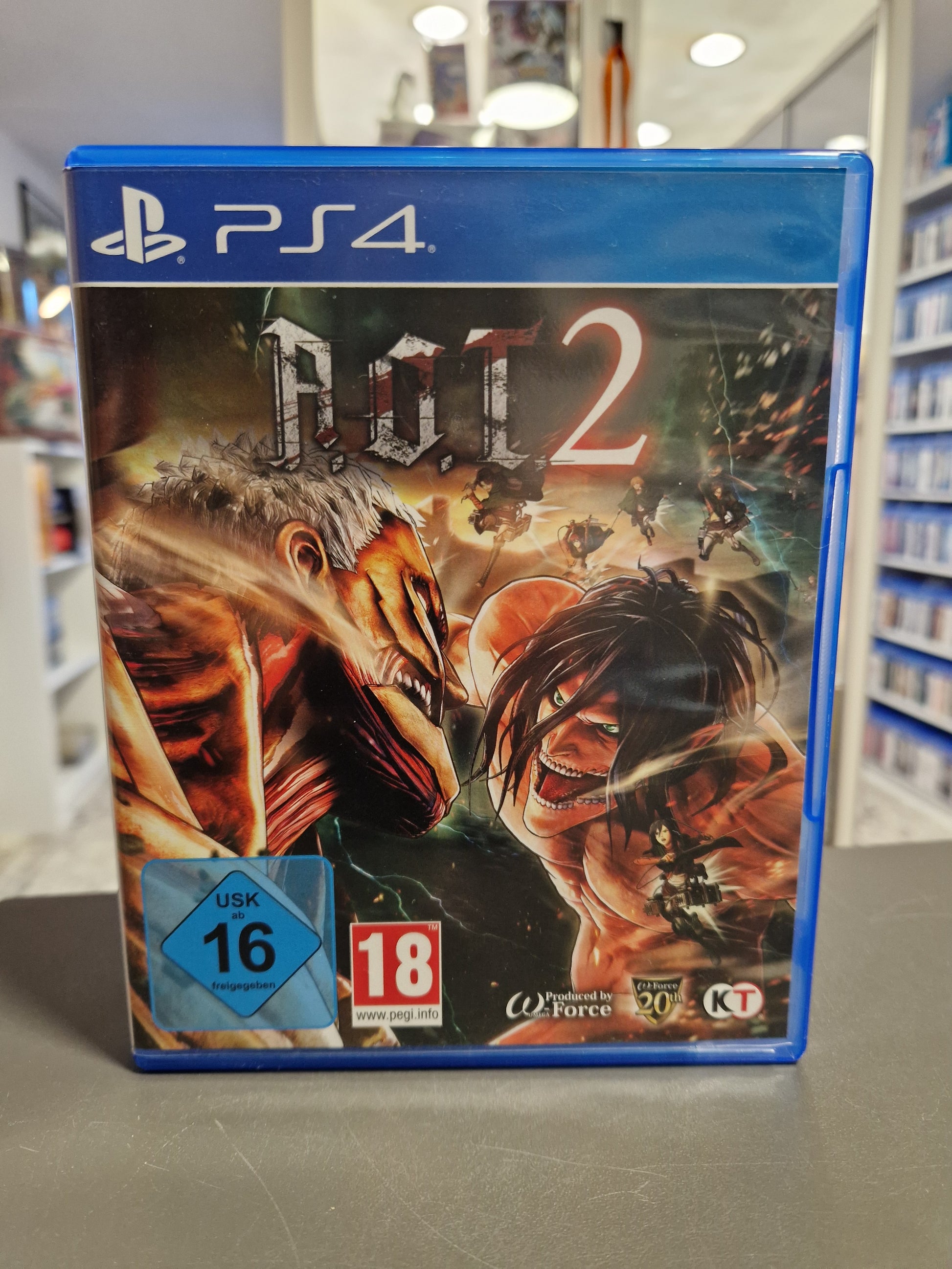 Vorderseite der PS4-Hülle von A.O.T. 2 (Attack on Titan 2). Das Cover zeigt einen dramatischen Kampf zwischen Titanen und Jägern. USK 16 und PEGI 18 Logos sind deutlich sichtbar.