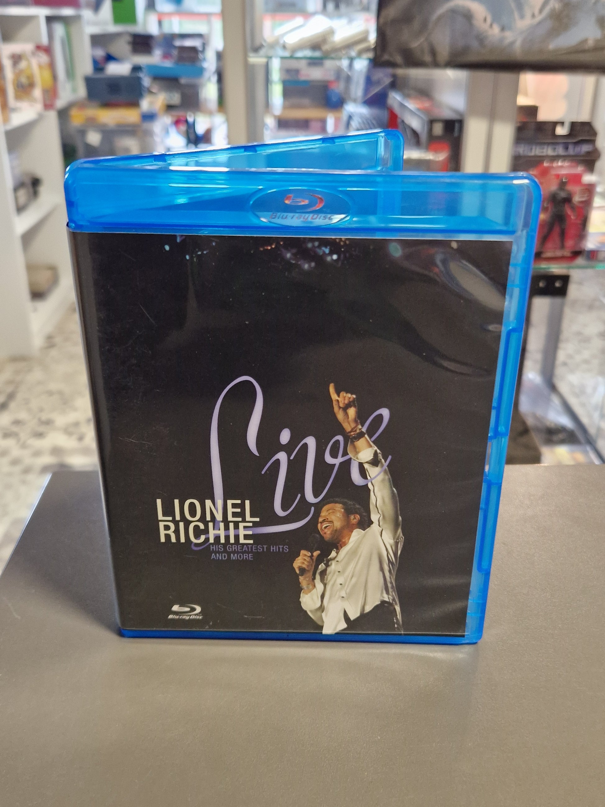 Vorderseite der Blu-ray Hülle von Lionel Richie Live His Greatest Hits and More auf schwarzem Hintergrund mit einem Foto des Sängers im weißen Hemd am Mikrofon.