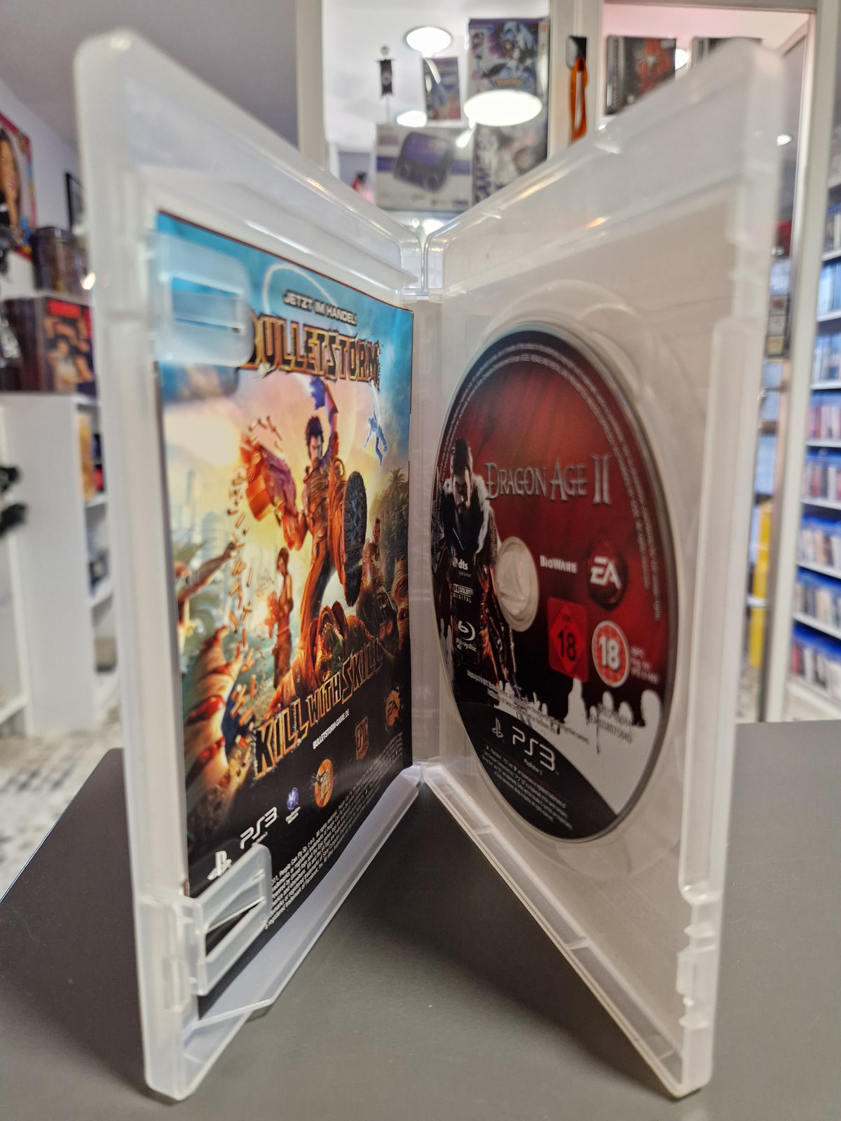 Geöffnete PlayStation 3 Hülle von Dragon Age II mit Blu-ray Disc und Flyern.