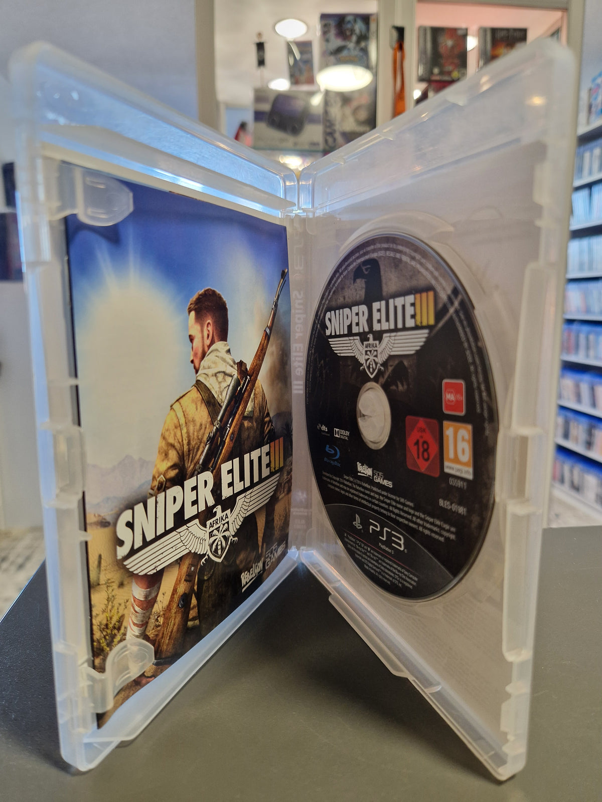Geöffnete PS3 Spielehülle von Sniper Elite III mit Blu-ray Disc und Anleitungsheft.