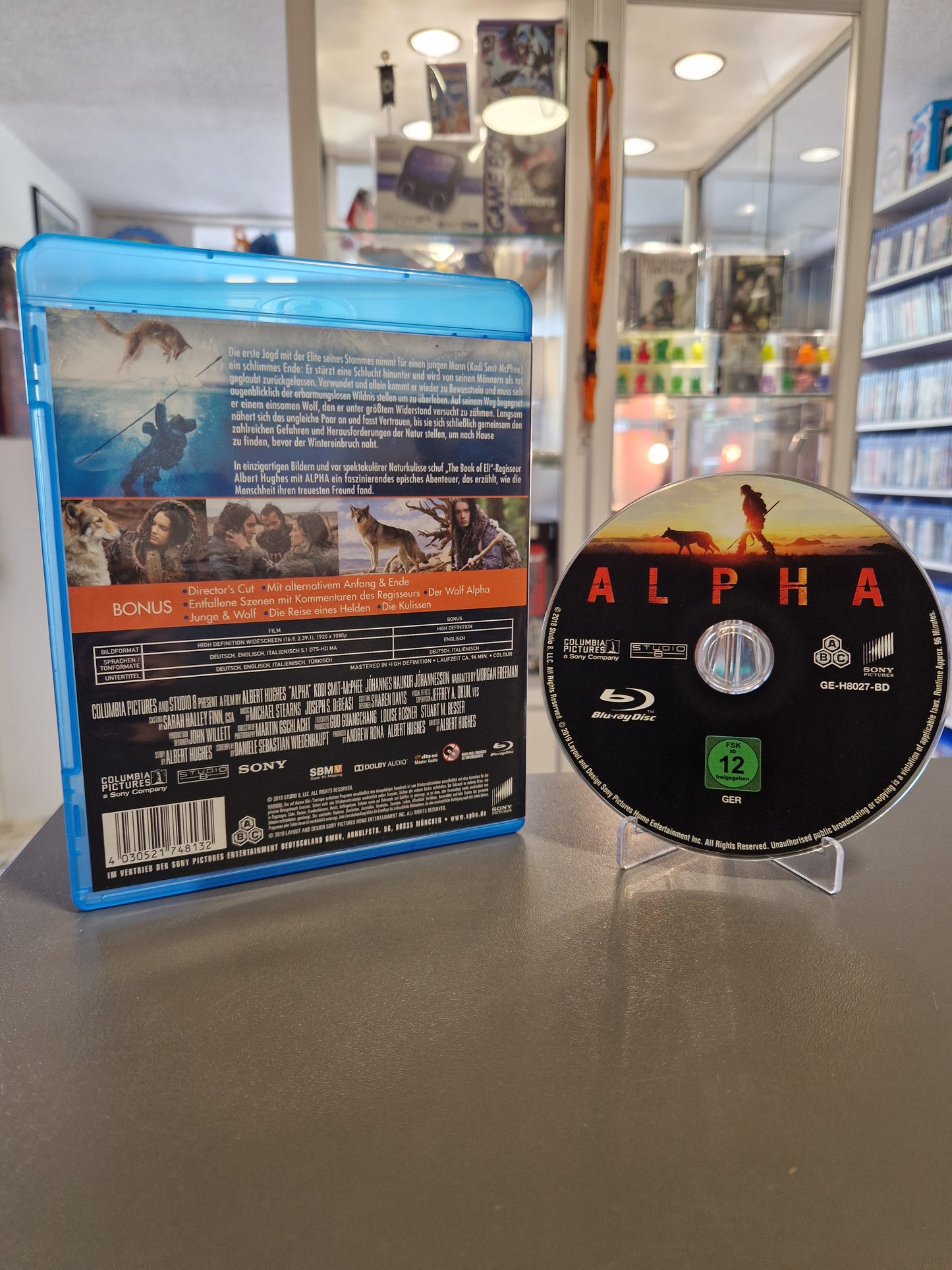 Rückseite der Alpha Blu-ray Verpackung mit der Inhaltsangabe, einer Liste der Bonusinhalte (wie dem Director's Cut), vier Filmausschnitten und den technischen Spezifikationen inklusive Barcode.