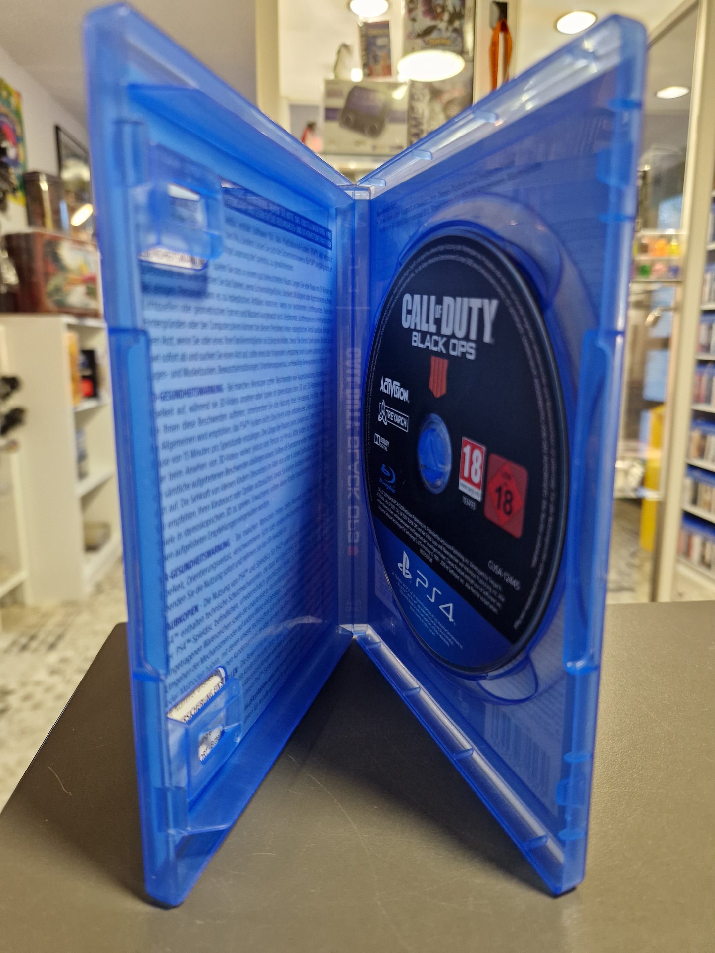 Innenansicht der PlayStation 4 Hülle von Black Ops 4 mit der eingelegten Spiel-Disc. Die Disc ist schwarz mit weißer Beschriftung. Links sind Gesundheitswarnungen im Inlay zu sehen.