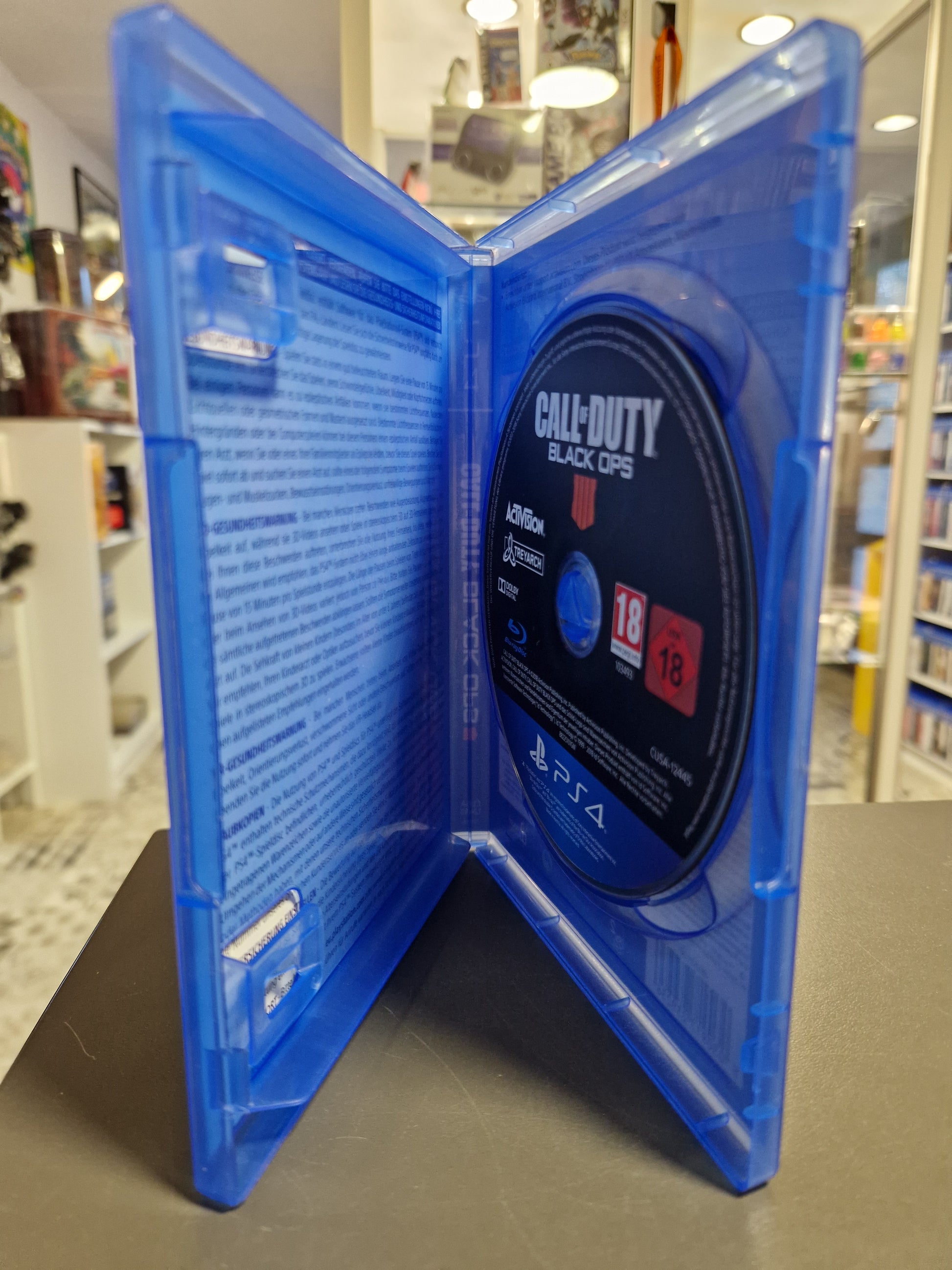 Innenansicht der PlayStation 4 Hülle von Black Ops 4 mit der eingelegten Spiel-Disc. Die Disc ist schwarz mit weißer Beschriftung. Links sind Gesundheitswarnungen im Inlay zu sehen.