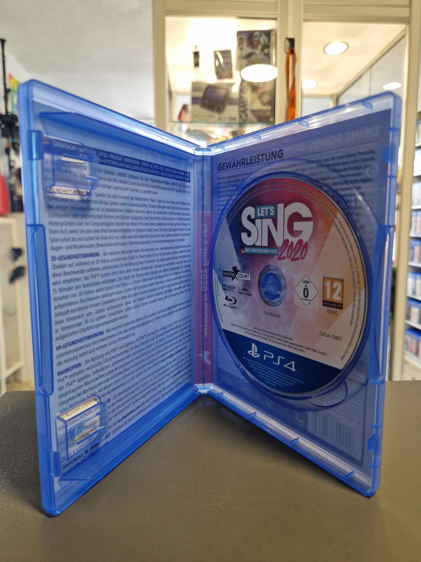 Die geöffnete blaue PlayStation 4 Kunststoffhülle zeigt die sicher im rechten Fach eingelegte Spiele-Disc von Let's Sing 2020 mit deutschen Hits.