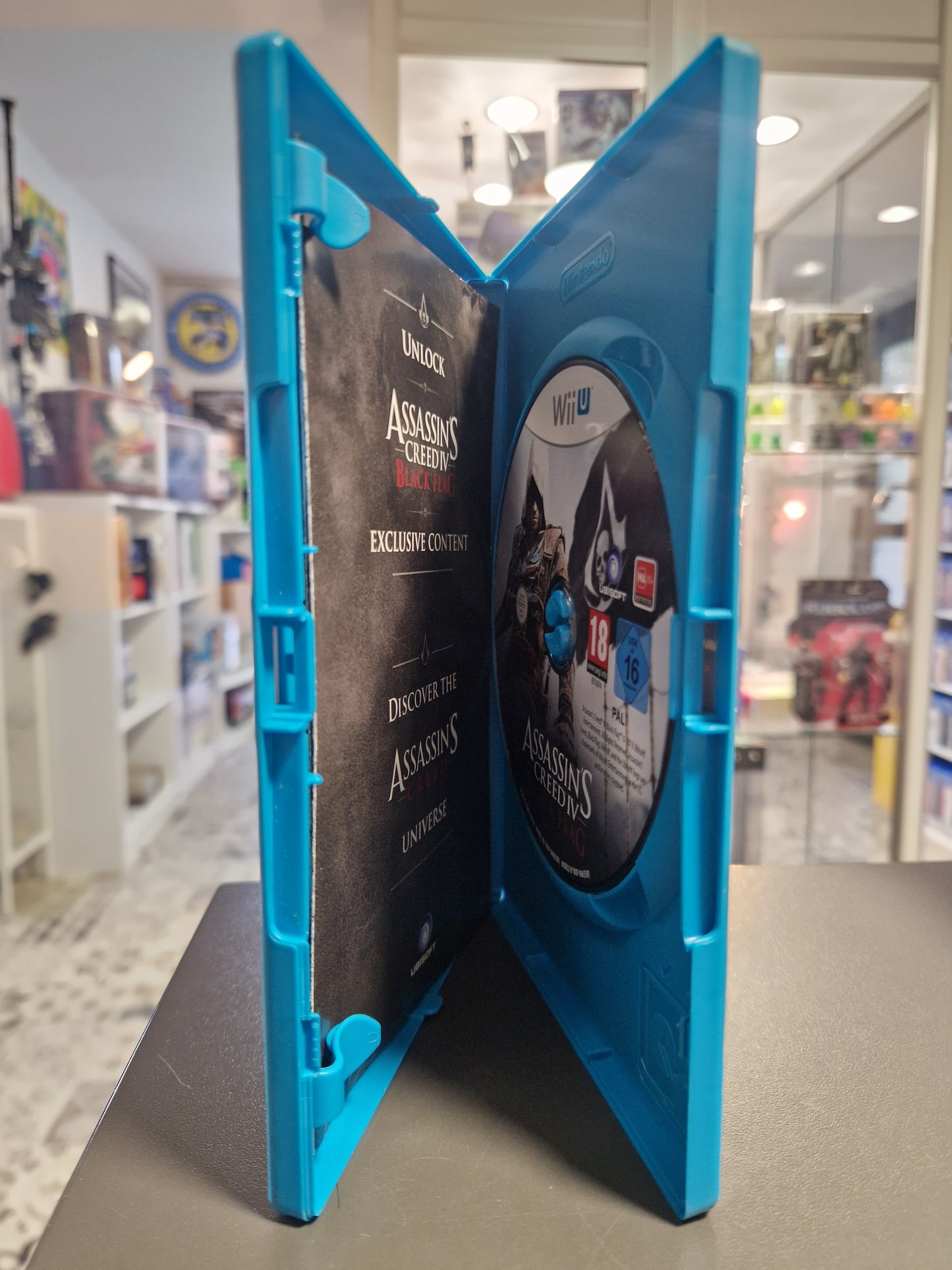 Geöffnete hellblaue Wii U Hülle mit der originalen Assassin's Creed IV Black Flag Spiele-Disc und der gedruckten Beilage im Laden Memory Lane in Rhauderfehn.