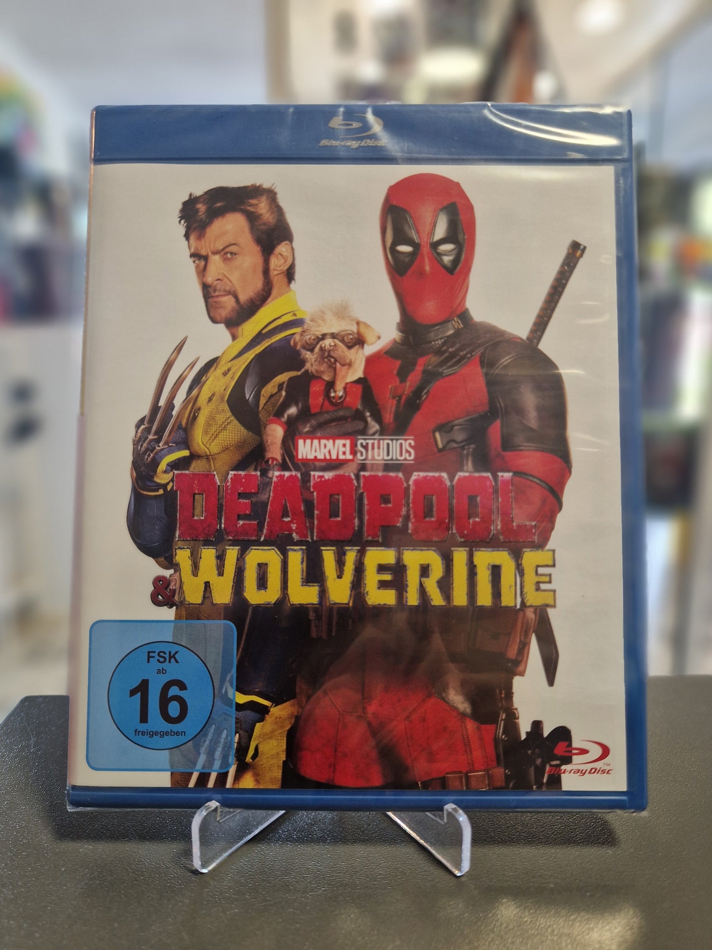 Die originalverschweißte Blu-ray-Hülle von Deadpool & Wolverine. Das Cover zeigt Hugh Jackman als Wolverine mit gezückten Krallen und Ryan Reynolds als Deadpool, der den kleinen Hund Dogpool im Arm hält. Unten links ist das blaue FSK 16 Logo zu sehen.