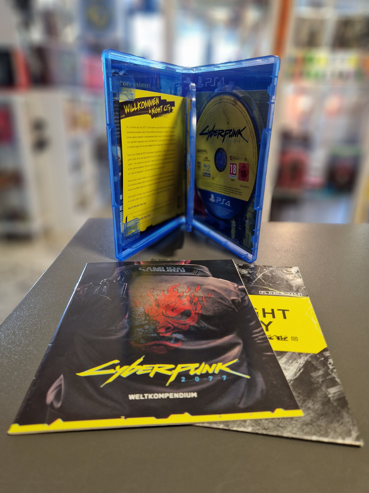 Aufgeklappte PS4 Hülle von Cyberpunk 2077 mit Discs, Weltkompendium und Stadtplan.