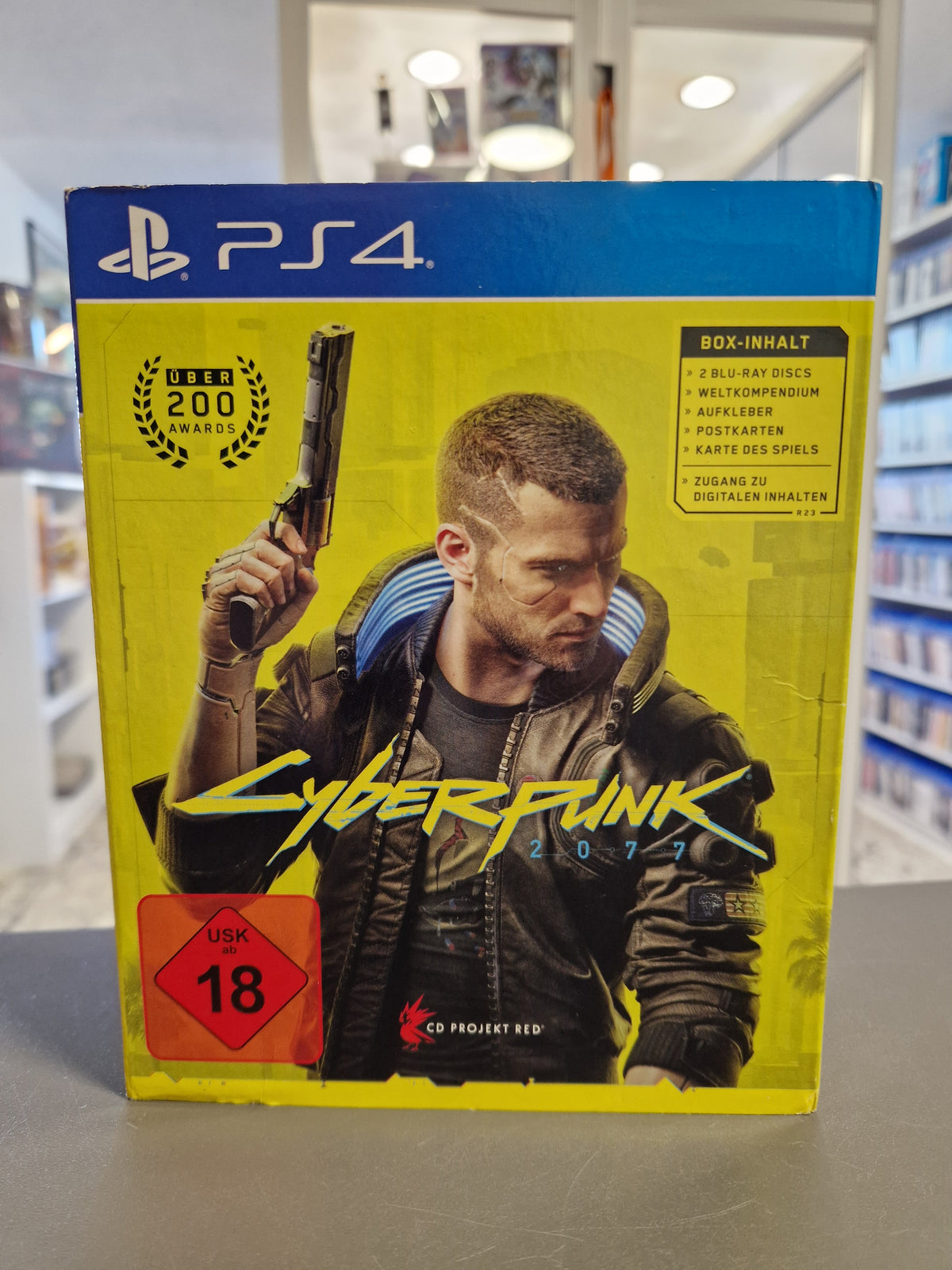 Vorderseite der Verpackung von Cyberpunk 2077 für PS4 im gelben Pappschuber.