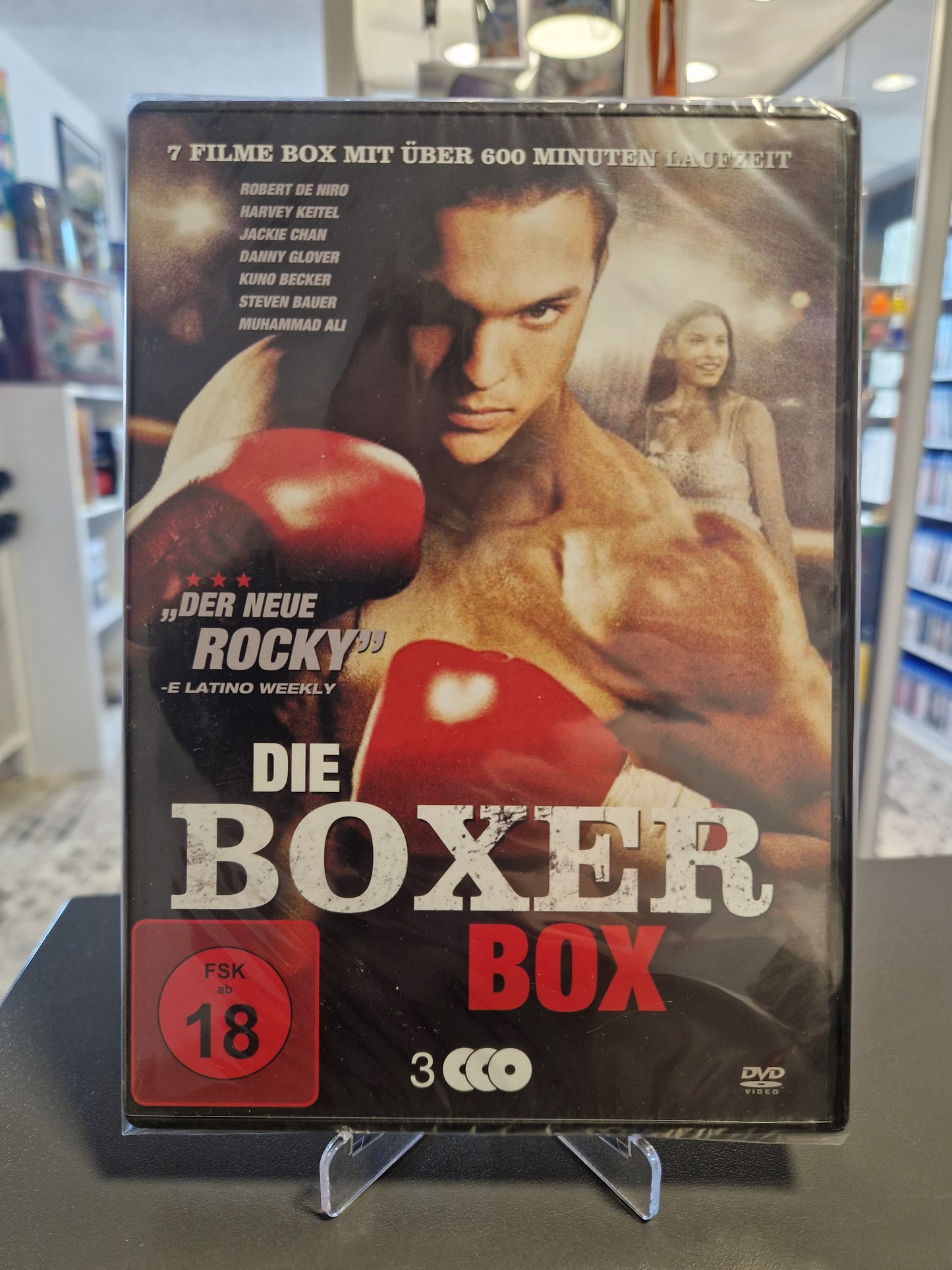 Neu und originalverpackte DVD-Sammlung Die Boxer Box mit FSK 18 Freigabe. Das Cover zeigt einen muskulösen Boxer mit roten Boxhandschuhen und listet Stars wie Robert De Niro, Jackie Chan und Muhammad Ali auf.