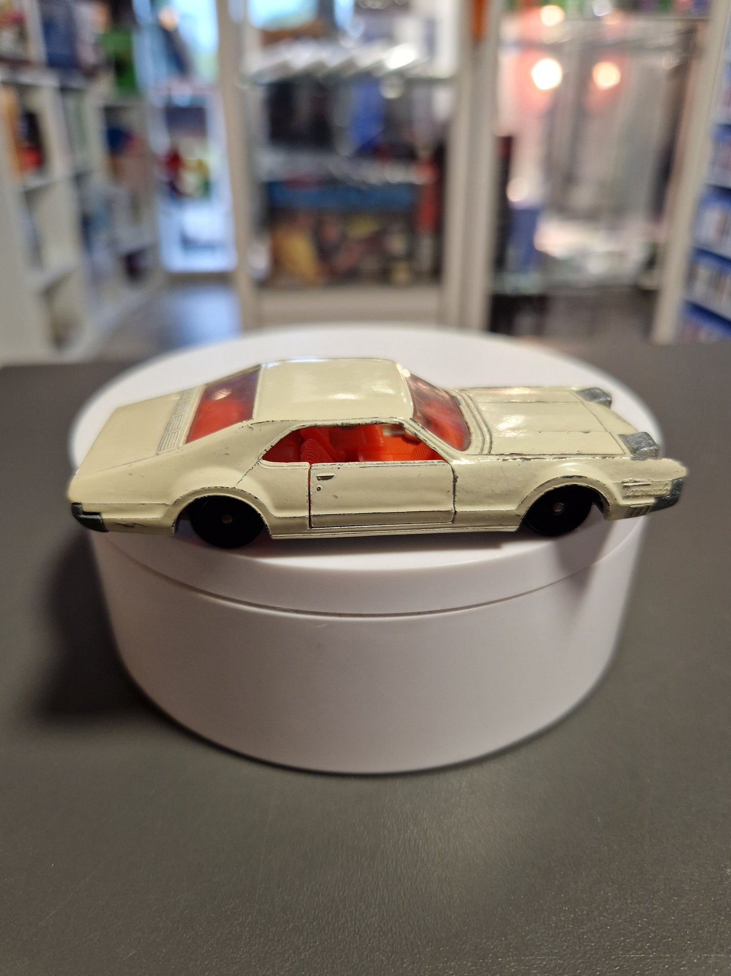 Seitenansicht eines cremeweißen Siku V 267 Oldsmobile Toronado Modellautos auf weißem Podest.