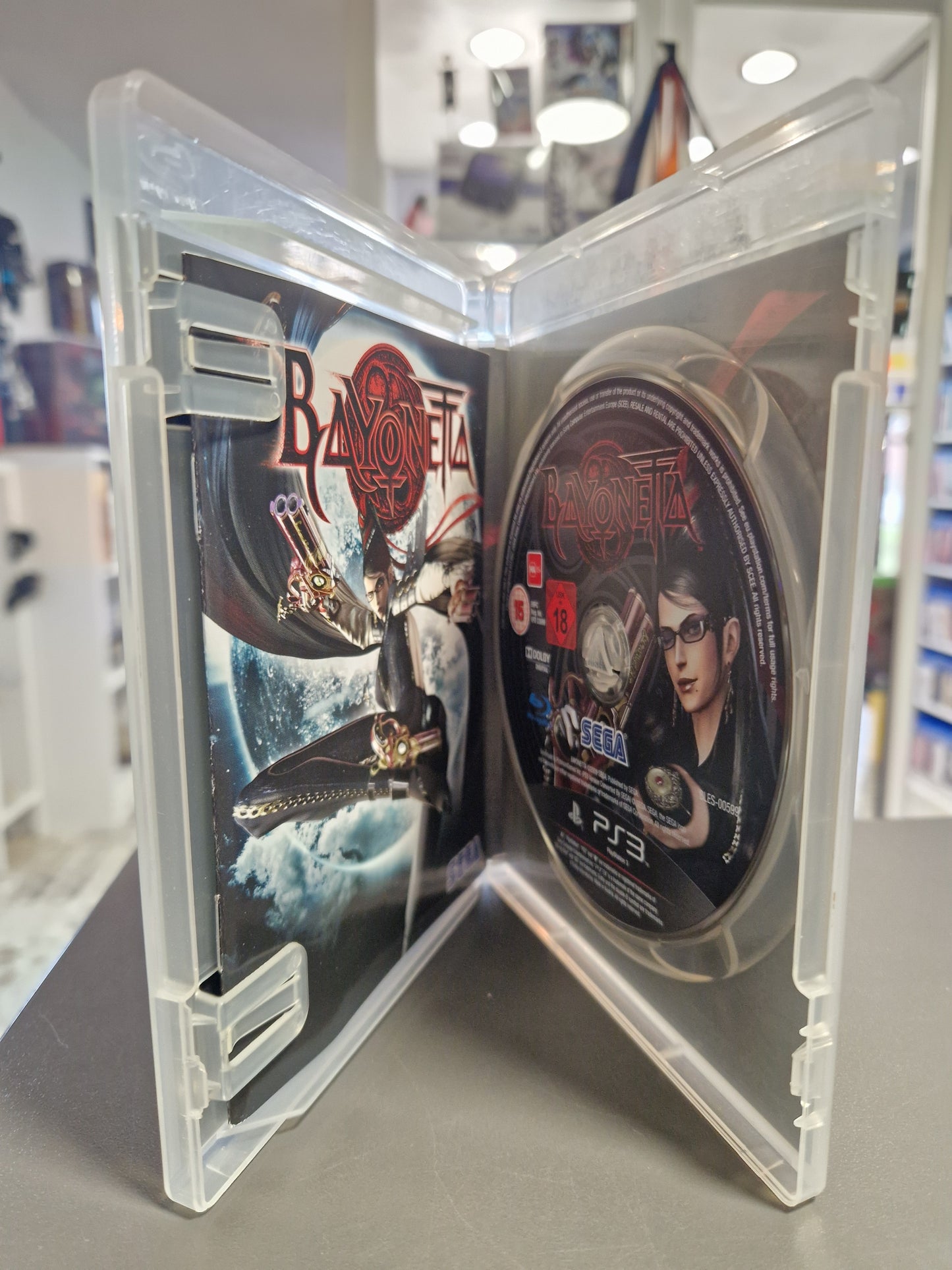 Geöffnete transparente PS3 Hülle von Bayonetta mit der bedruckten Spiel-Disc auf der rechten Seite und der gedruckten Anleitung auf der linken Seite.