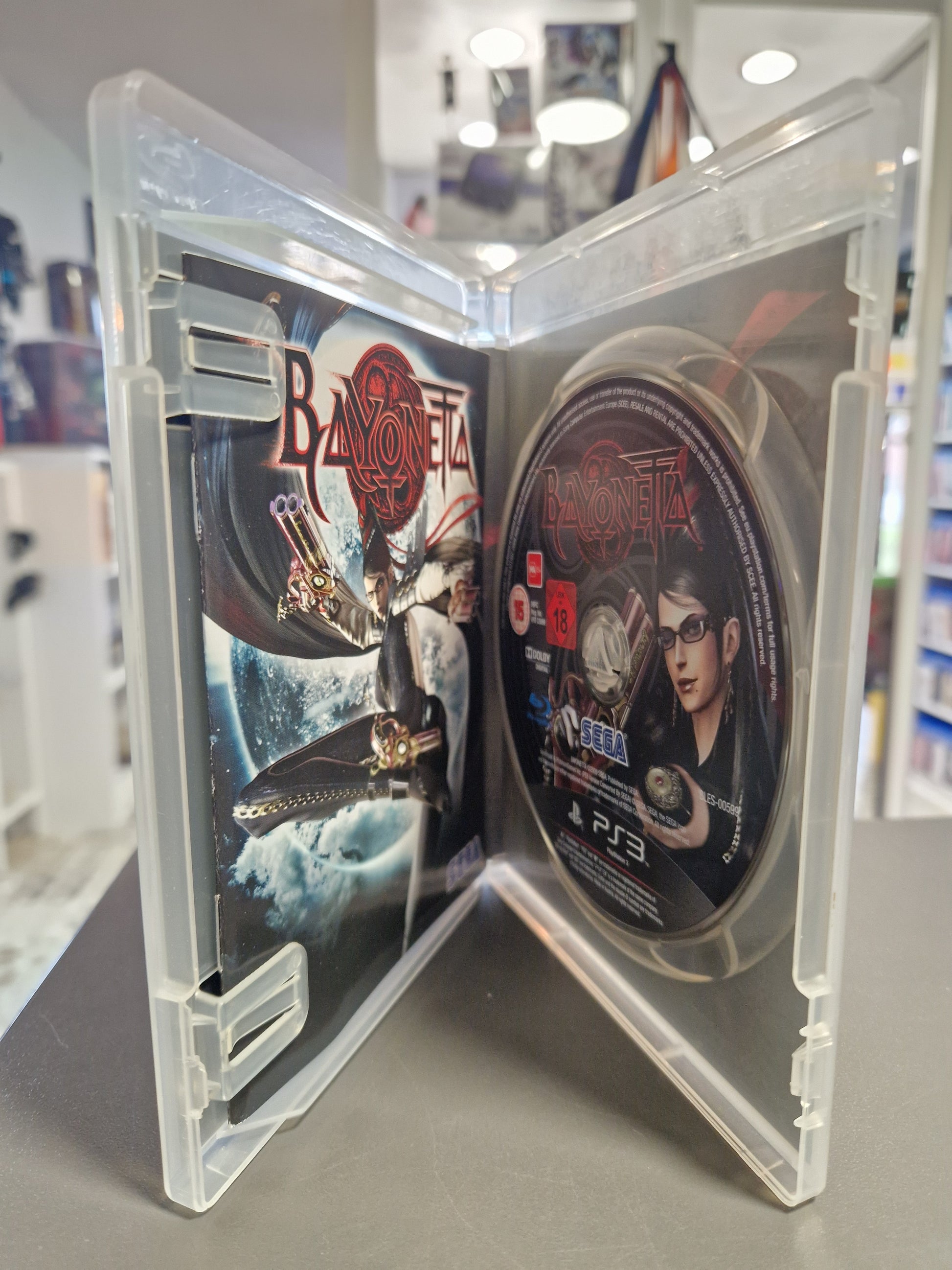 Geöffnete transparente PS3 Hülle von Bayonetta mit der bedruckten Spiel-Disc auf der rechten Seite und der gedruckten Anleitung auf der linken Seite.