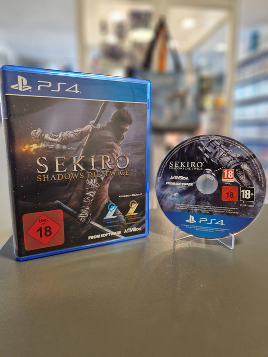 Die PlayStation 4 Hülle von Sekiro: Shadows Die Twice neben der originalen Blu-ray Spieldisc auf einem Aufsteller. Auf dem Cover ist der einarmige Shinobi mit gezogenem Katana zu sehen. Das rote USK 18 Logo ist deutlich sichtbar.