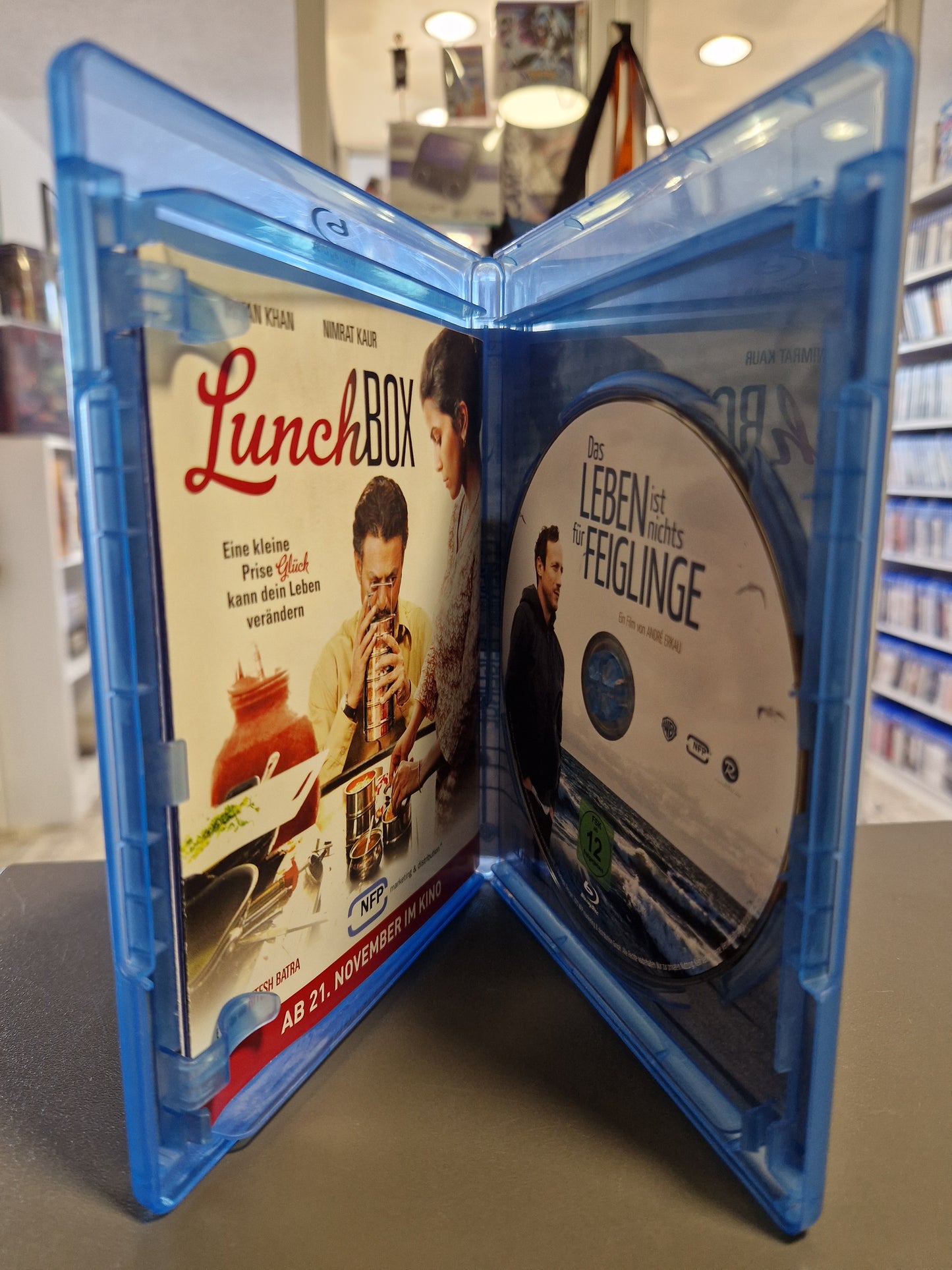 Geöffnete blaue Blu-ray Hülle mit der Filmdisc von Das Leben ist nichts für Feiglinge auf der rechten Seite und dem eingelegten Lunchbox-Flyer auf der linken Seite.