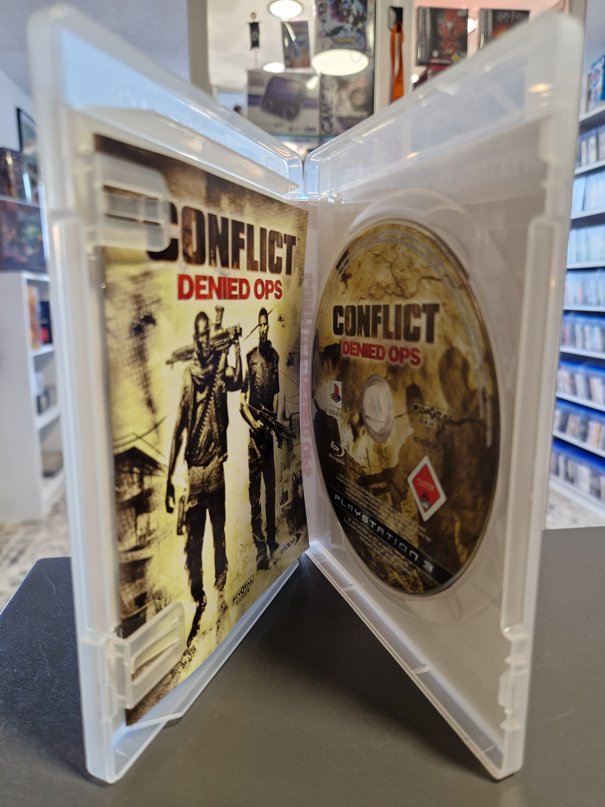 Geöffnete PS3 Hülle von Conflict Denied Ops mit Spiel-Disc und gedrucktem Booklet.