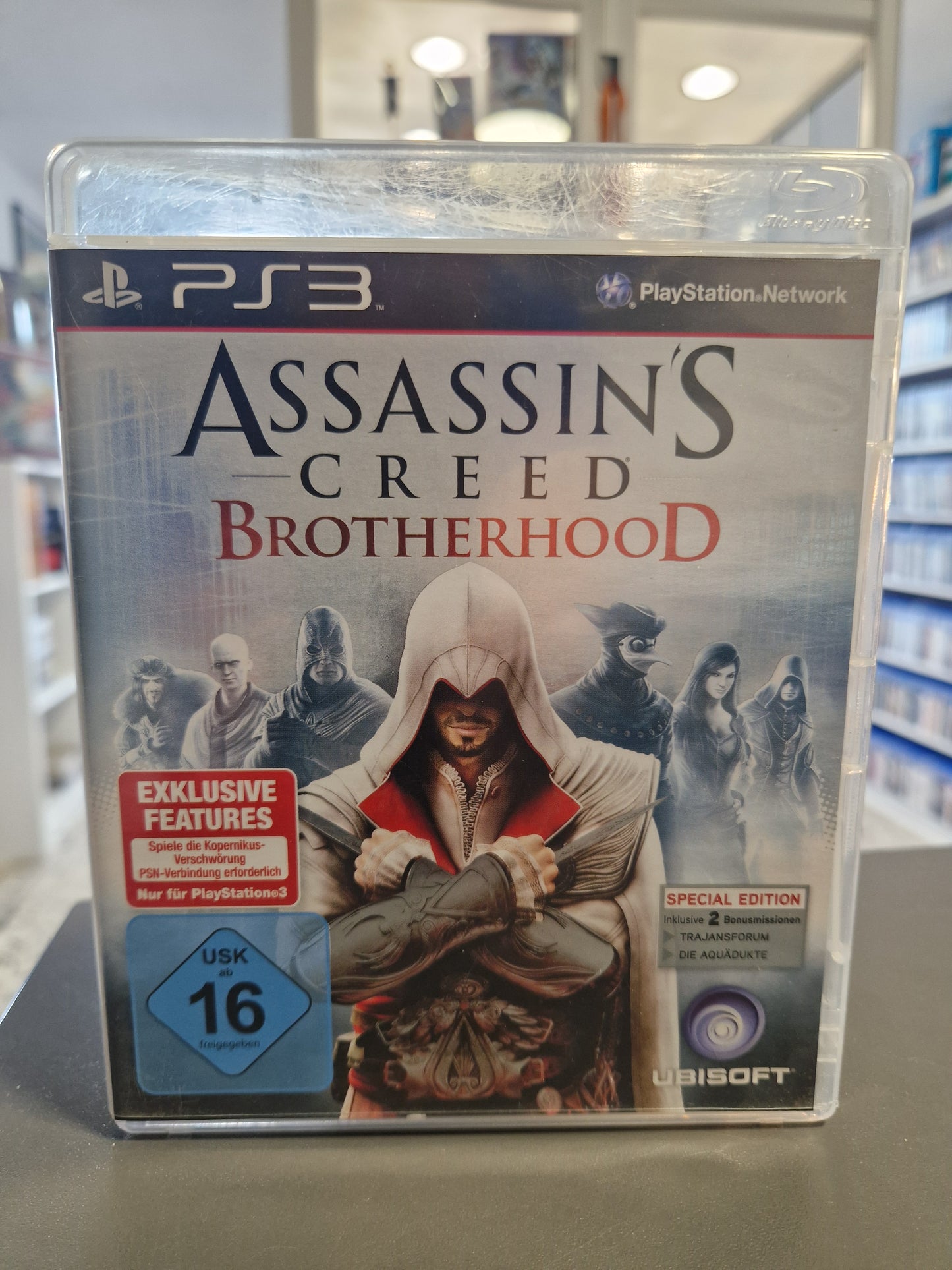 PS3-Cover von „Assassin's Creed: Brotherhood“ zeigt Ezio Auditore da Firenze in seiner weißen Assassinen-Robe, flankiert von seinen Verbündeten im historischen Rom.
