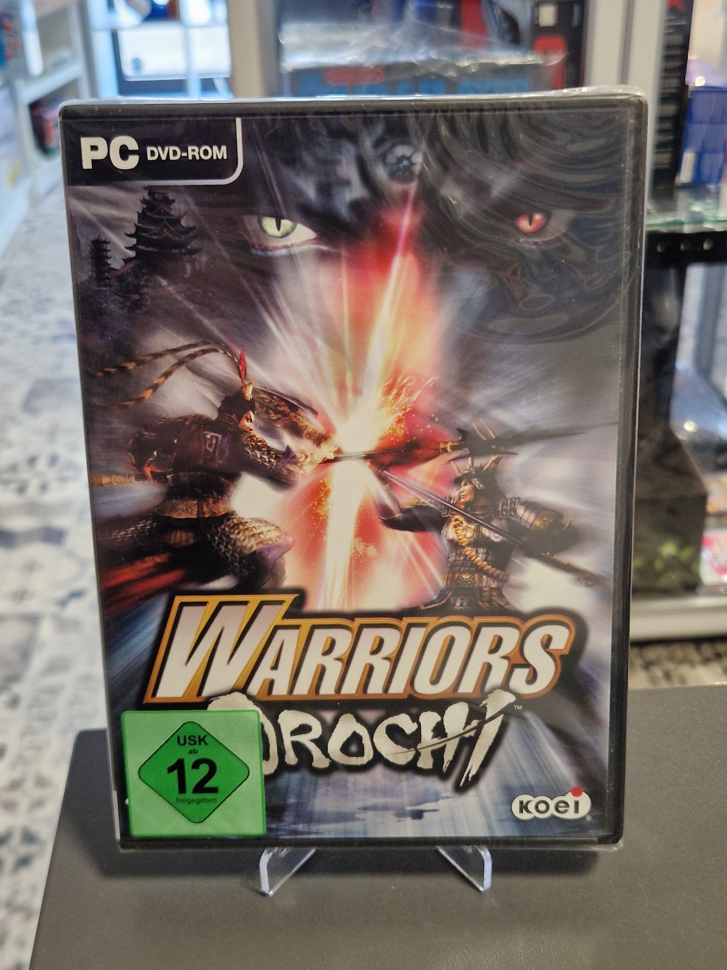 Frontcover der PC-DVD-Hülle von „Warriors Orochi“ in Originalfolie, zeigt zwei legendäre Krieger beim Aufeinandertreffen ihrer Waffen.