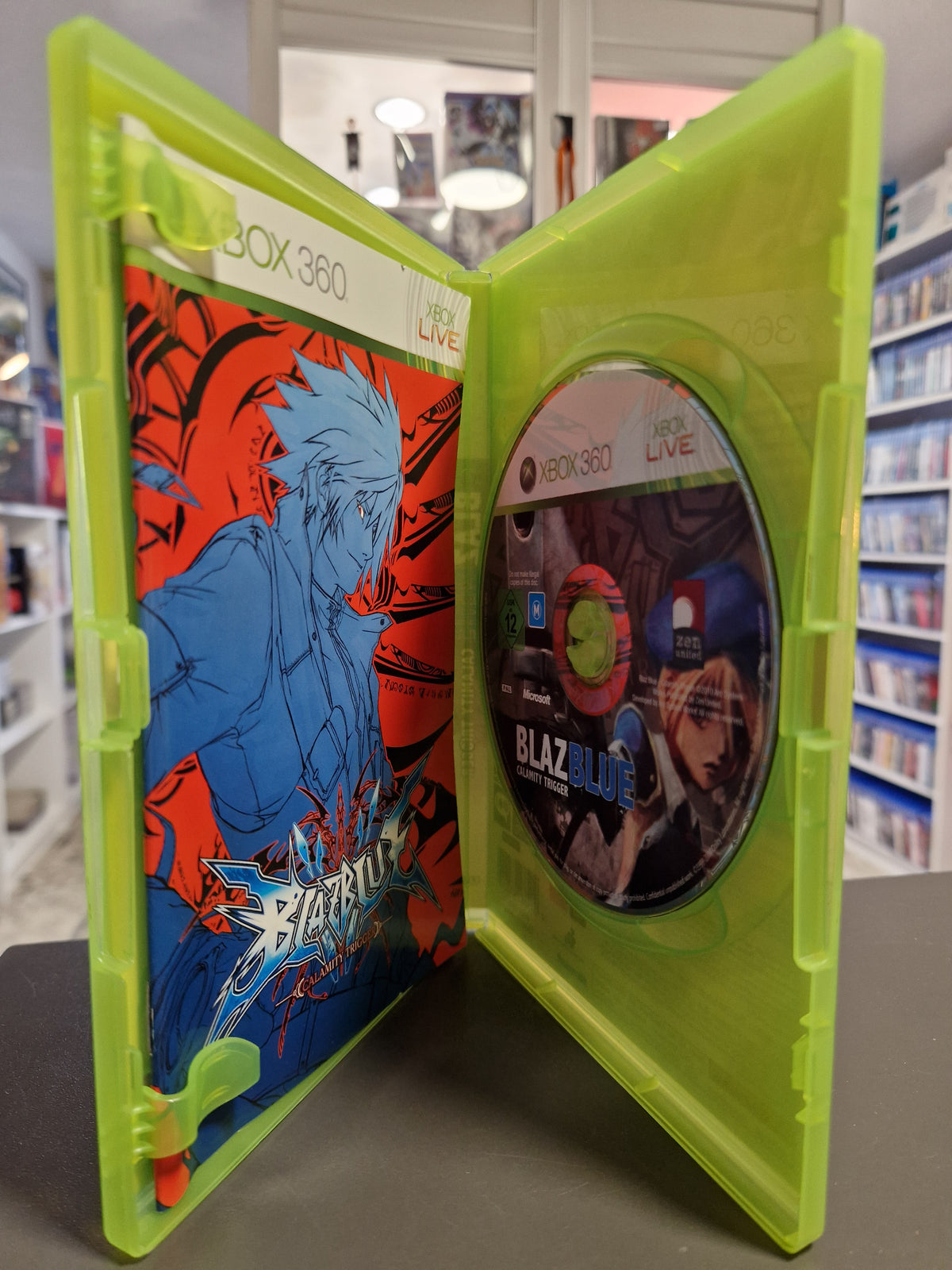 Geöffnete Xbox 360 Hülle von BlazBlue Calamity Trigger mit Disc und gedrucktem Booklet.