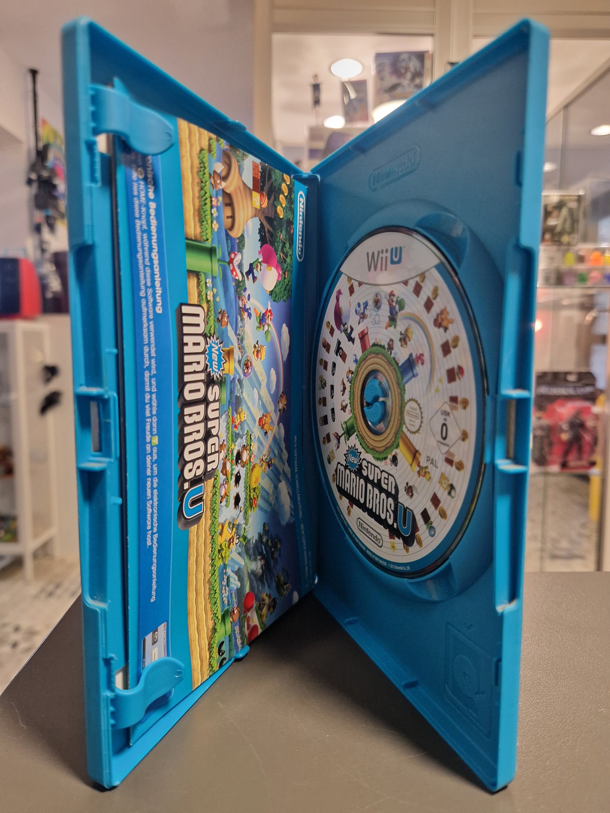 Geöffnete blaue Wii U Hülle von New Super Mario Bros U mit Spiele-Disc und gedruckter Anleitung