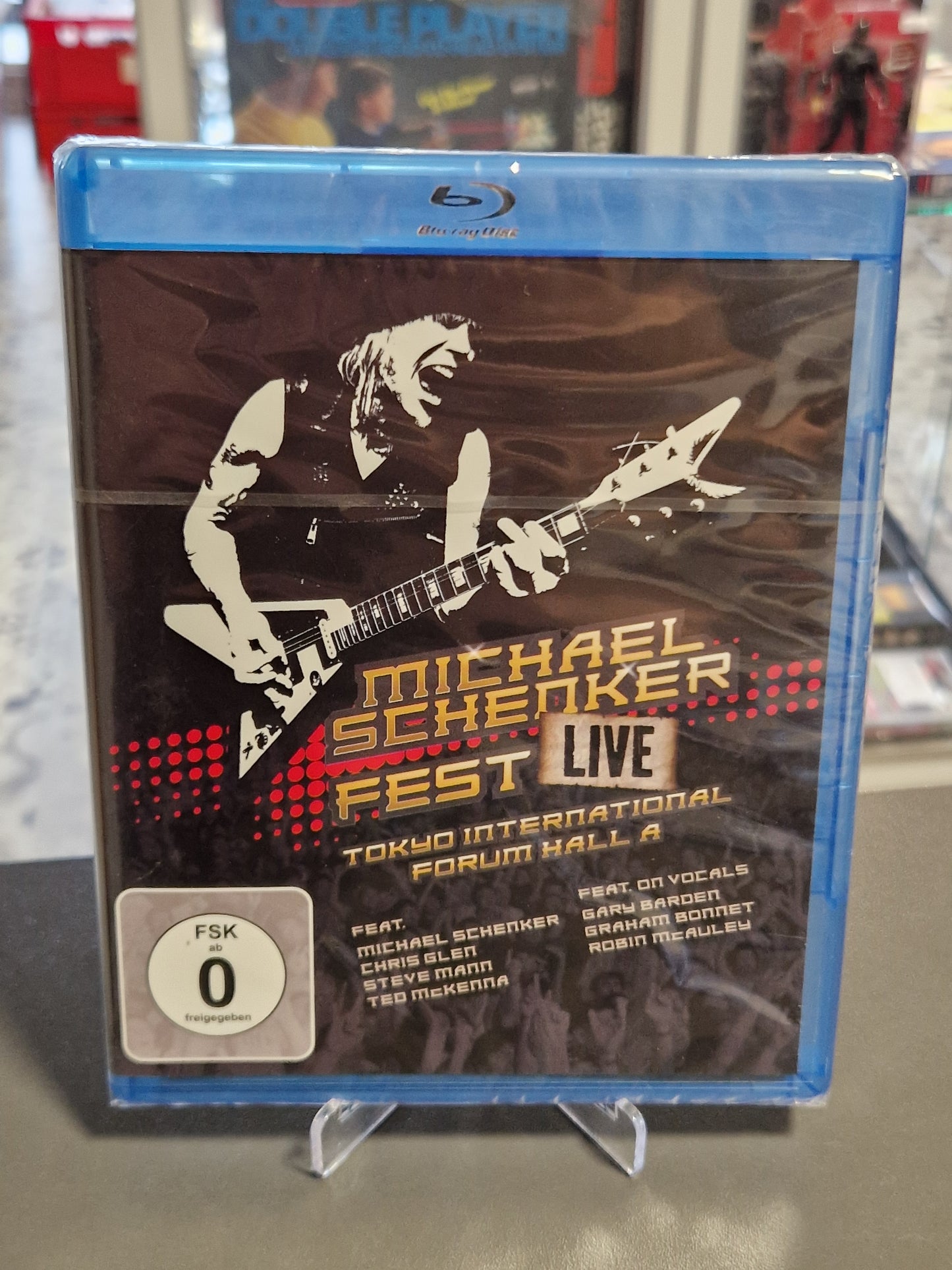 Vorderseite der originalverpackten Blu-ray Hülle von Michael Schenker Fest Live Tokyo International Forum Hall A mit einer stilisierten Grafik des Gitarristen auf dunklem Grund und weißem FSK 0 Logo.