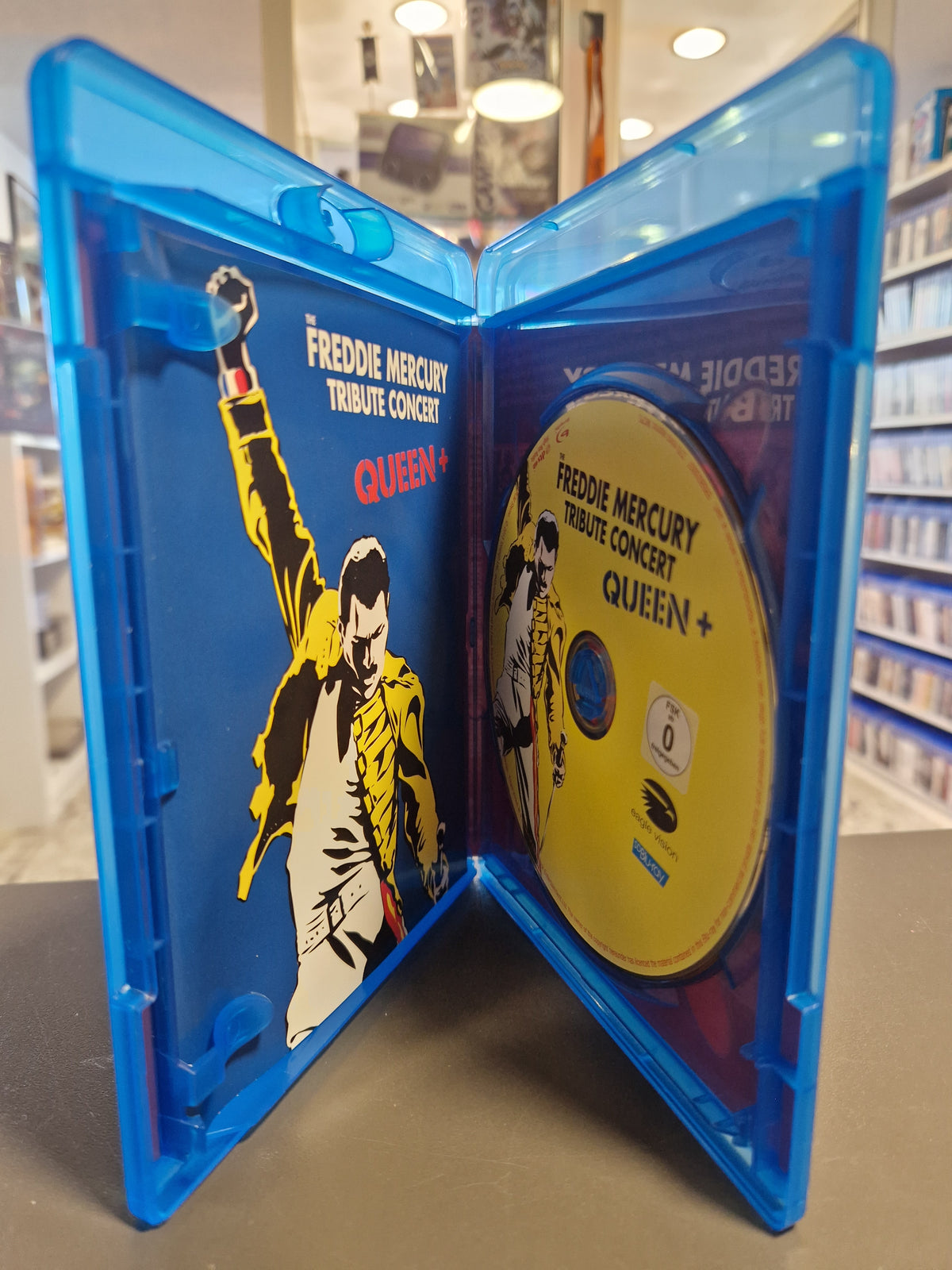 Geöffnete Blu-ray Hülle von The Freddie Mercury Tribute Concert mit gelber Disc und Booklet.
