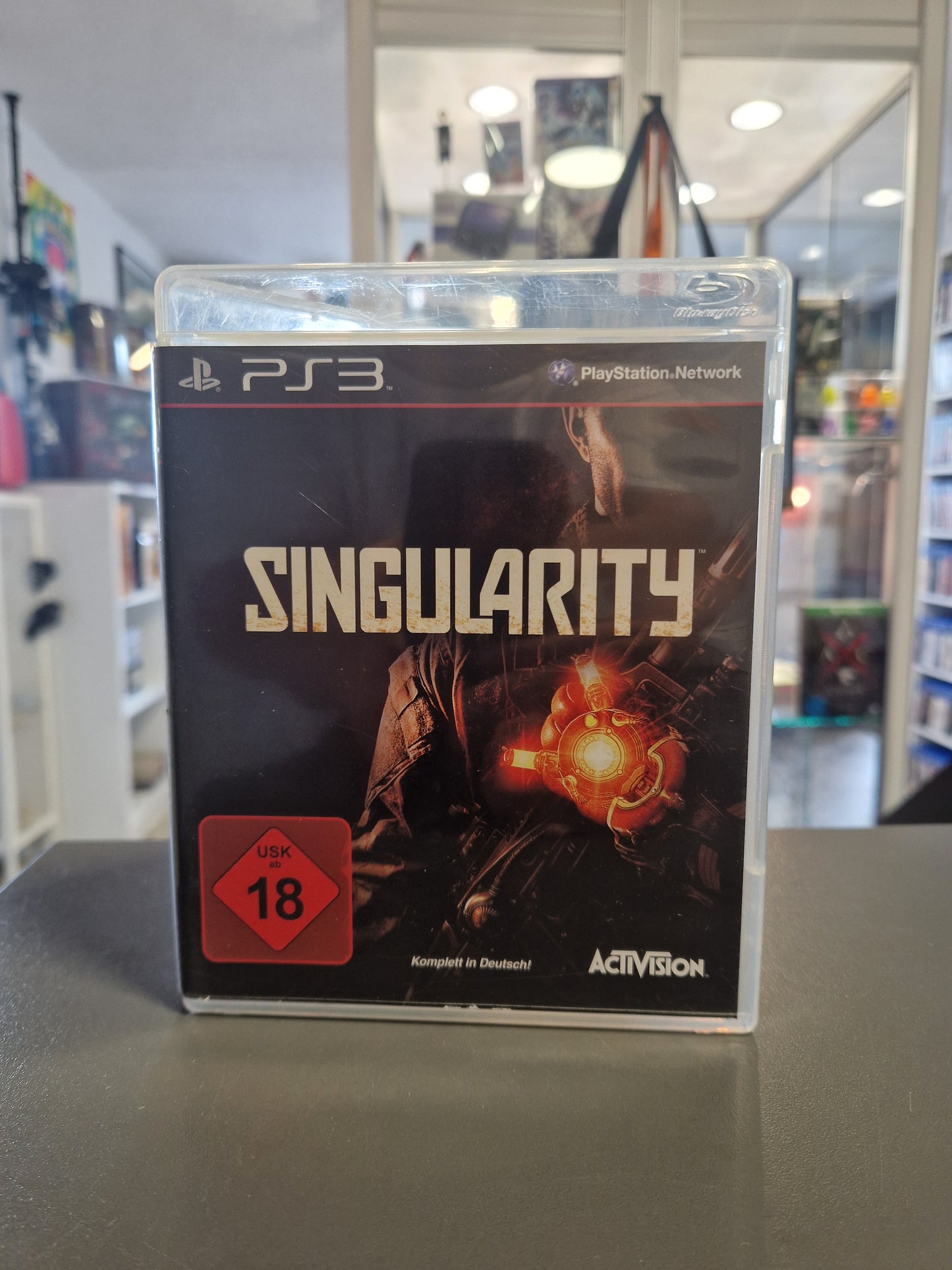 Die PlayStation 3 Spielehülle von Singularity mit dem roten USK 18 Logo. Auf dem dunklen Cover ist ein Soldat mit einem leuchtend orangefarbenen Zeitmanipulationsgerät an der Hand zu sehen.