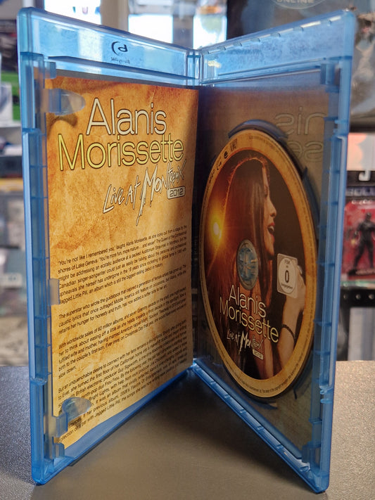 Geöffnete Blu-ray Hülle von Alanis Morissette Live at Montreux 2012 mit der goldfarbenen Konzert-Disc auf der rechten Seite und dem aufgeschlagenen Inlay-Booklet mit englischem Begleittext auf der linken Seite.