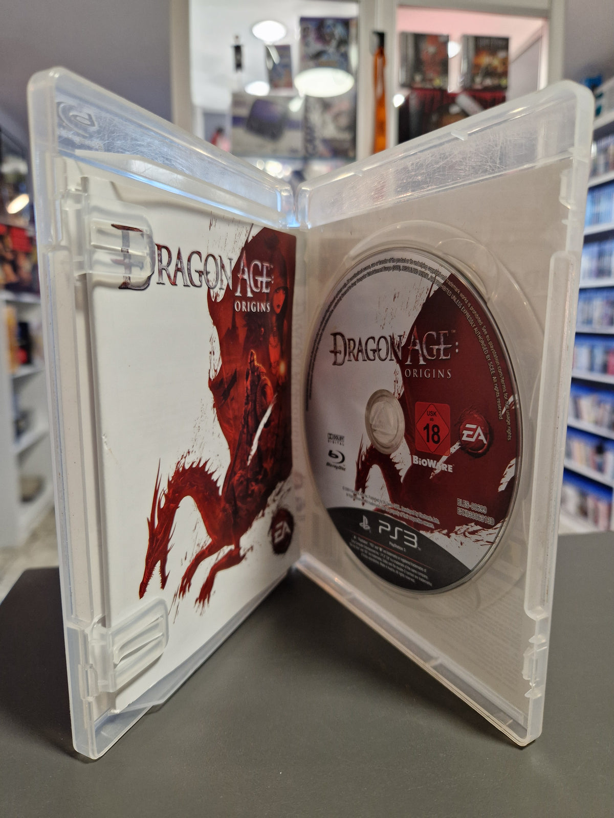 Geöffnete PlayStation 3 Hülle von Dragon Age Origins mit Blu-ray Disc und Anleitung.