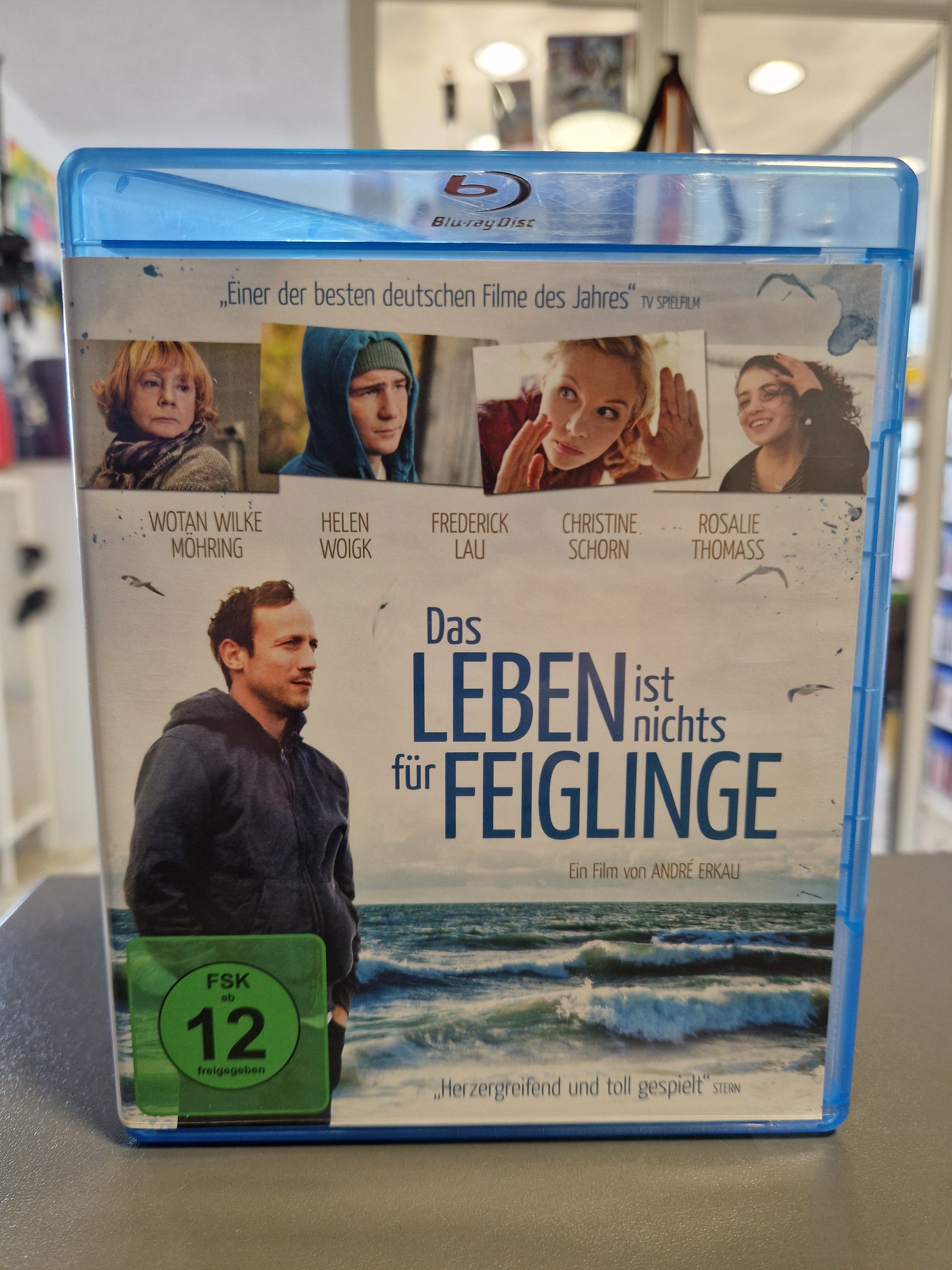 Vorderseite der Blu-ray Hülle von Das Leben ist nichts für Feiglinge mit Darsteller Wotan Wilke Möhring vor einem Meereshintergrund und dem grünen FSK 12 Logo.