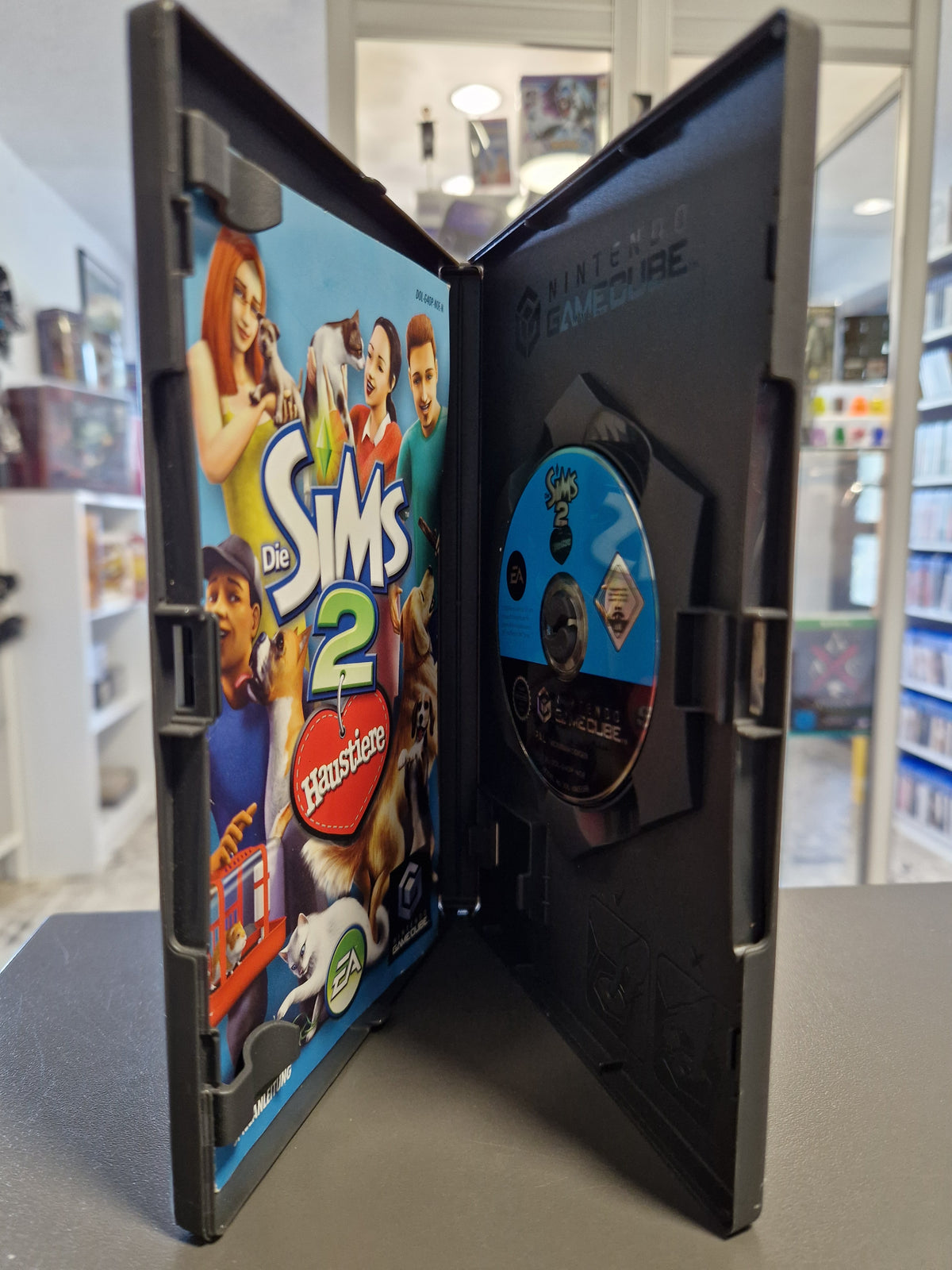 Geöffnete Nintendo GameCube Hülle von Die Sims 2 Haustiere mit Disc und gedruckter Spielanleitung.